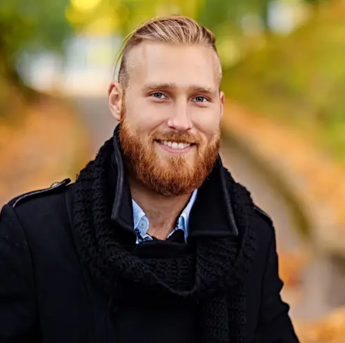 En smilende mann, stående utendørs i en høstpark.